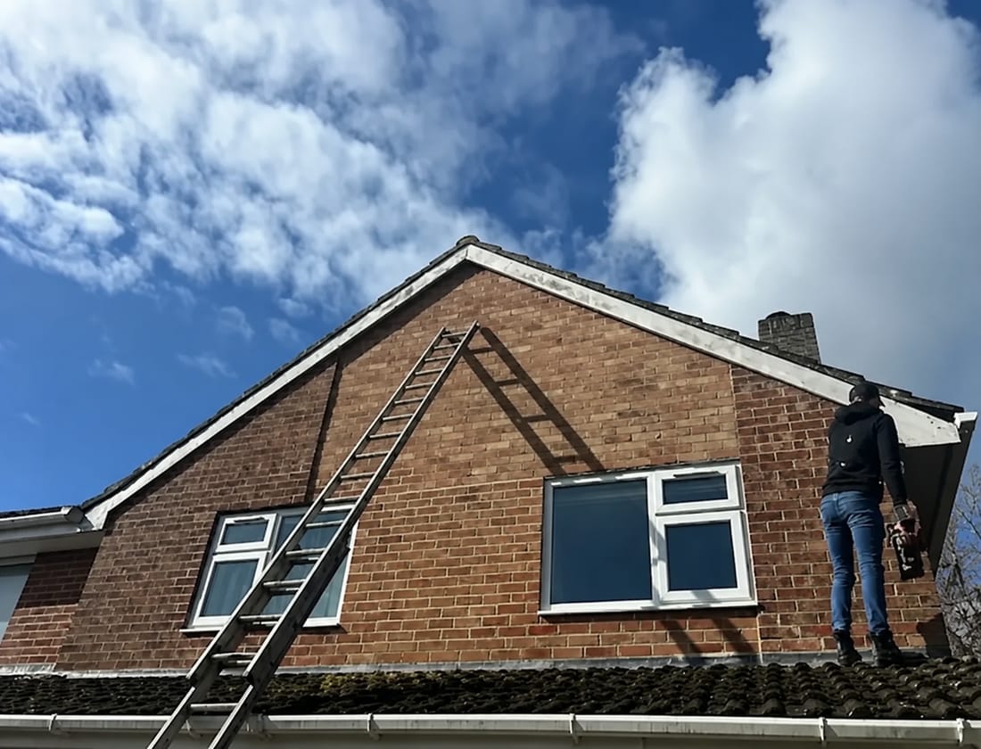 A CAW roofer working on a bargeboard from a ladder against a brick gable end
